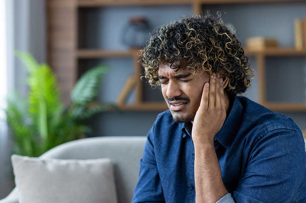 Man on a couch holding the side of his head over a clogged ear feeling, a concern at Eastside Audiology & Hearing Services in Issaquah, WA